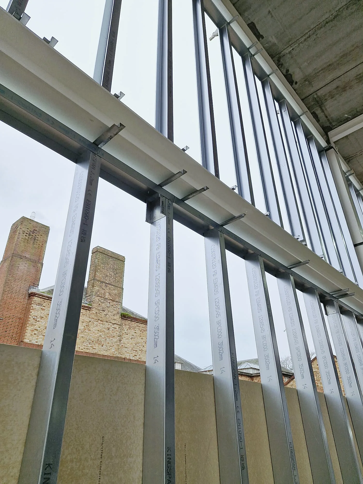 Tall steel studs fixed under a steel beam, with boards below